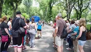A group of people is attentively listening to a tour guide in a lush park setting.