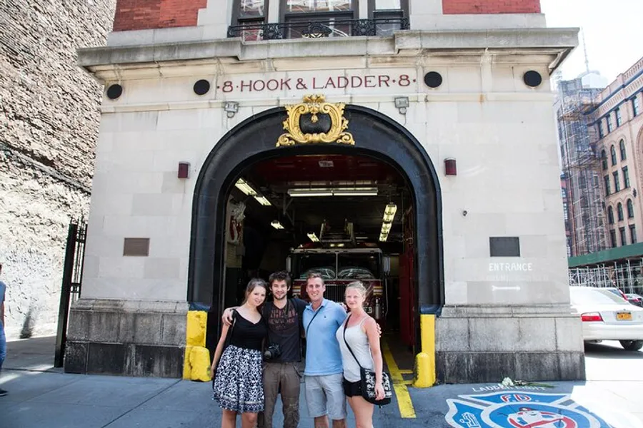 Three people are posing for a photo in front of the Hook & Ladder 8 firehouse, known for its appearance in the Ghostbusters movies.