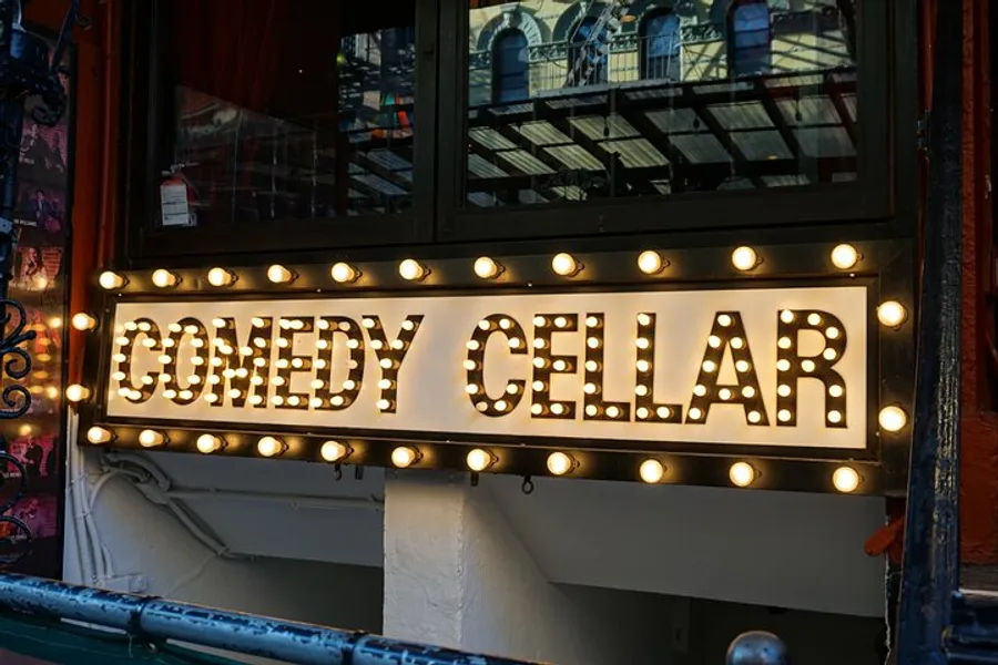 The image shows a lit-up marquee with the words COMEDY CELLAR, suggesting it is the entrance to a comedy club.