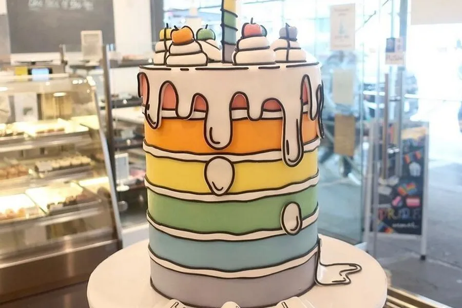 This image shows a multi-tiered, colorful cake decorated with dripping icing details and topped with what appears to be edible decorations resembling fruits.