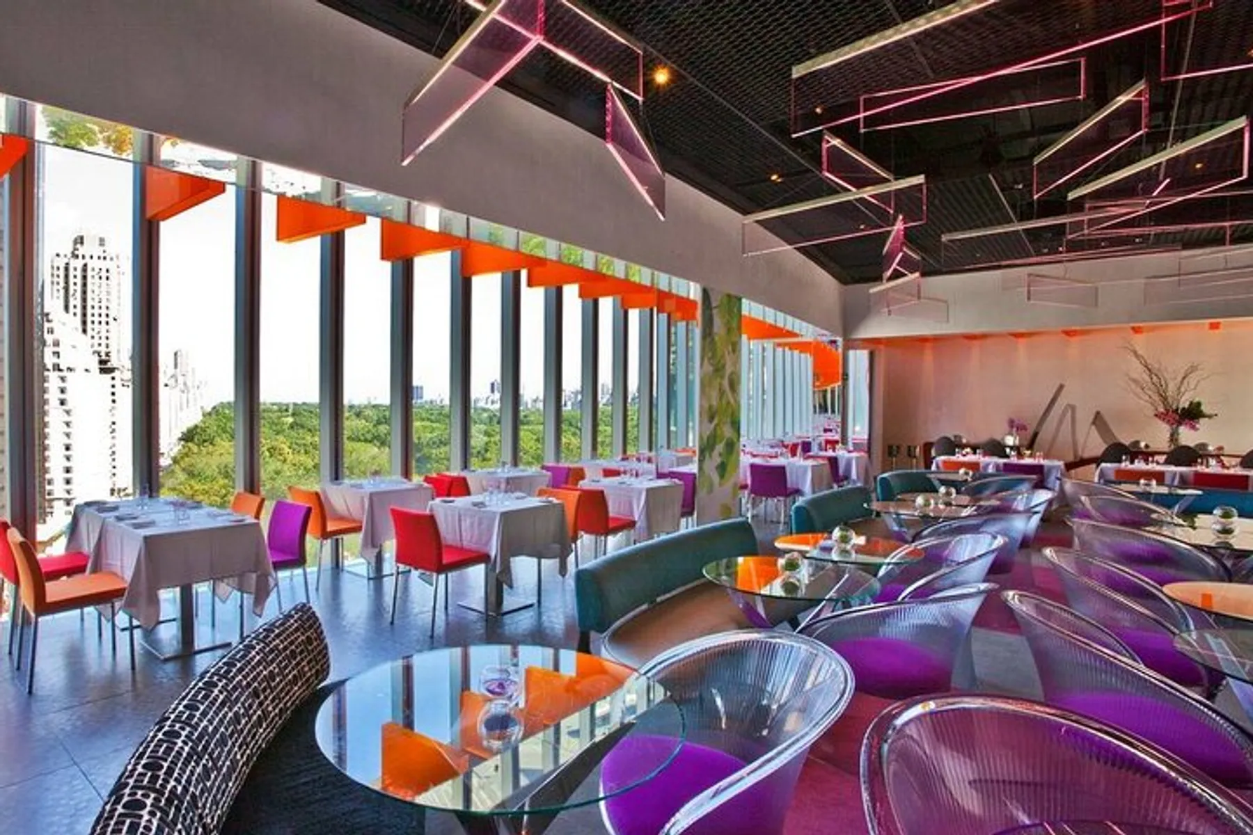 The image shows a modern restaurant interior with vibrant colors, contemporary furnishings, and large windows that offer plenty of natural light.
