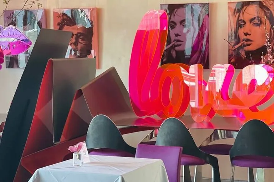 The image shows a modern and artistically decorated interior of a cafe or restaurant with vibrant sculptures and artwork, featuring bold representations of the word love and stylized portraits.