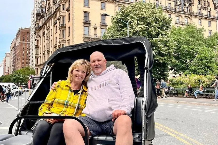 A smiling man and woman are sitting in a pedicab with city buildings and trees in the background.