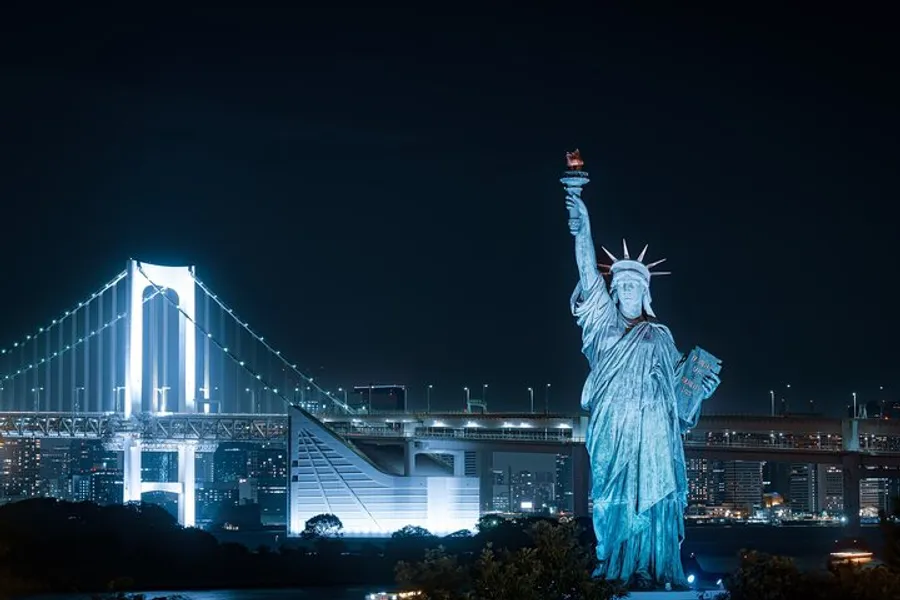The image features a replica of the Statue of Liberty with a backdrop of a lit suspension bridge at night.