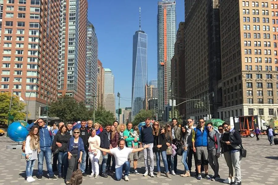 A group of people is posing for a photo on a sunny day with the One World Trade Center in the background.
