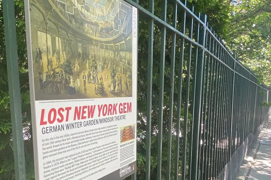 The image shows an information plaque titled LOST NEW YORK GEM German Winter Garden/Windsor Theatre mounted on a metal fence along a sidewalk with greenery in the background.