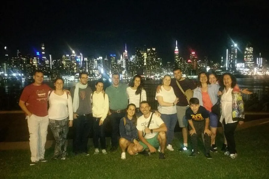A group of people is posing for a photo at night with a brightly lit city skyline in the background.