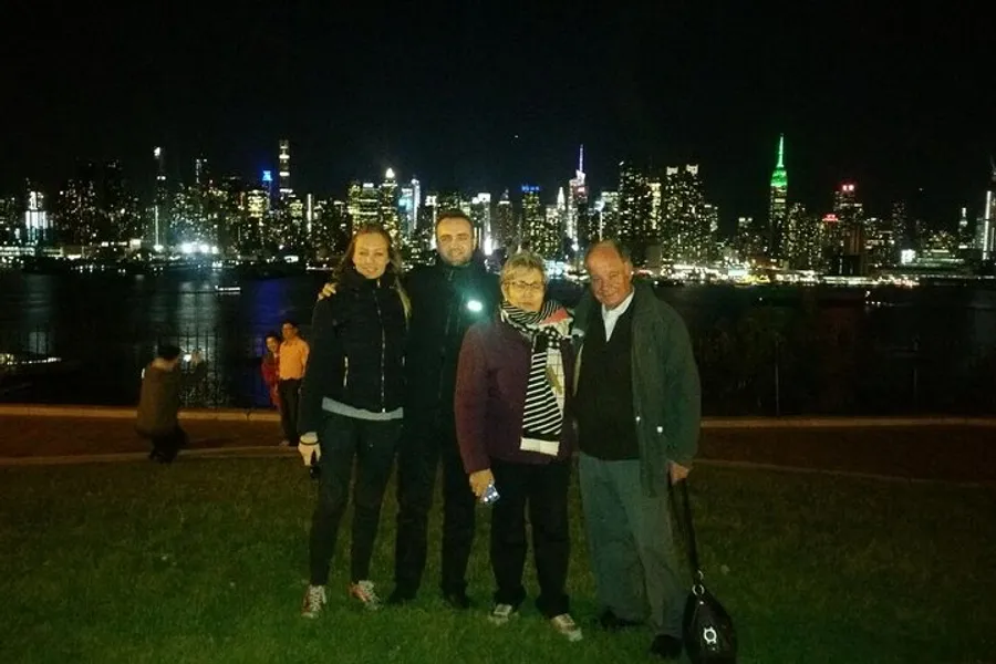 Four people are posing for a photo at night with a brightly lit city skyline in the background.