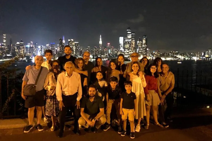 A group of people pose for a nighttime photo with a brightly lit city skyline in the background.