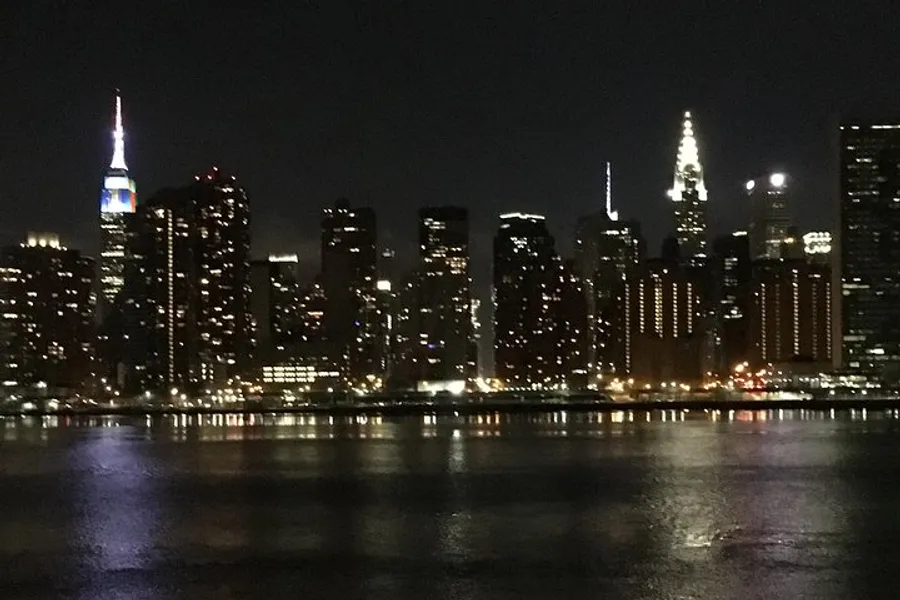 A nighttime view of a city skyline with illuminated buildings reflecting on the water.