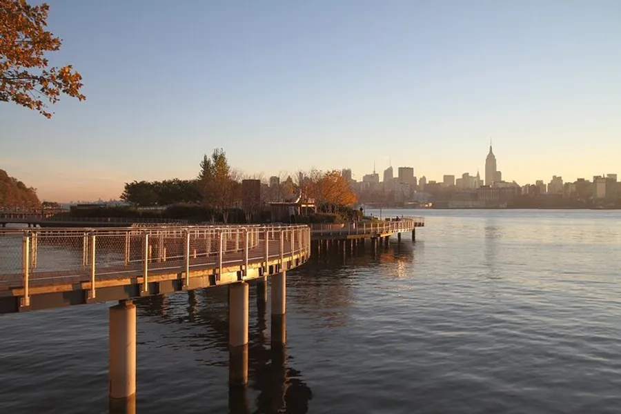 The image shows a serene waterfront pathway at sunset with a view of a city skyline in the background.