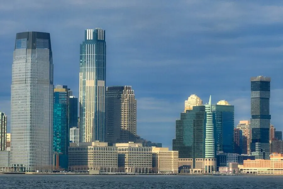 The image showcases a view of a modern city skyline with tall skyscrapers towering over the waterfront under a cloudy sky.