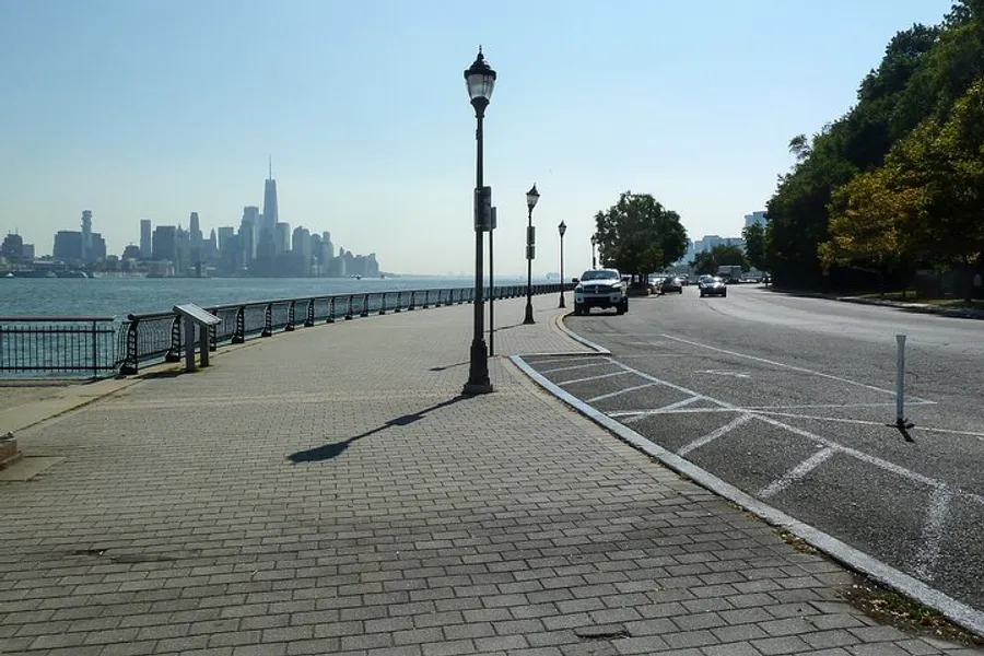 A riverside promenade with street lamps and a view of a distant city skyline on a sunny day.