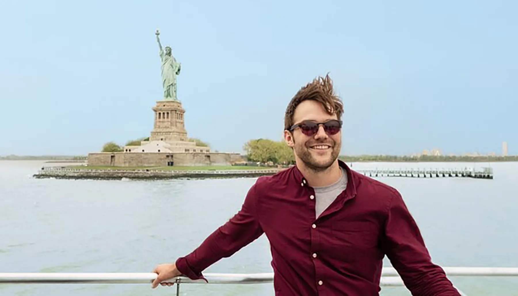 A smiling person is posing for a photo in front of the Statue of Liberty.