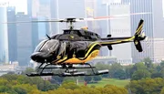 A black and yellow helicopter is flying in front of a city skyline backdrop with skyscrapers, possibly on a surveillance or transport mission.