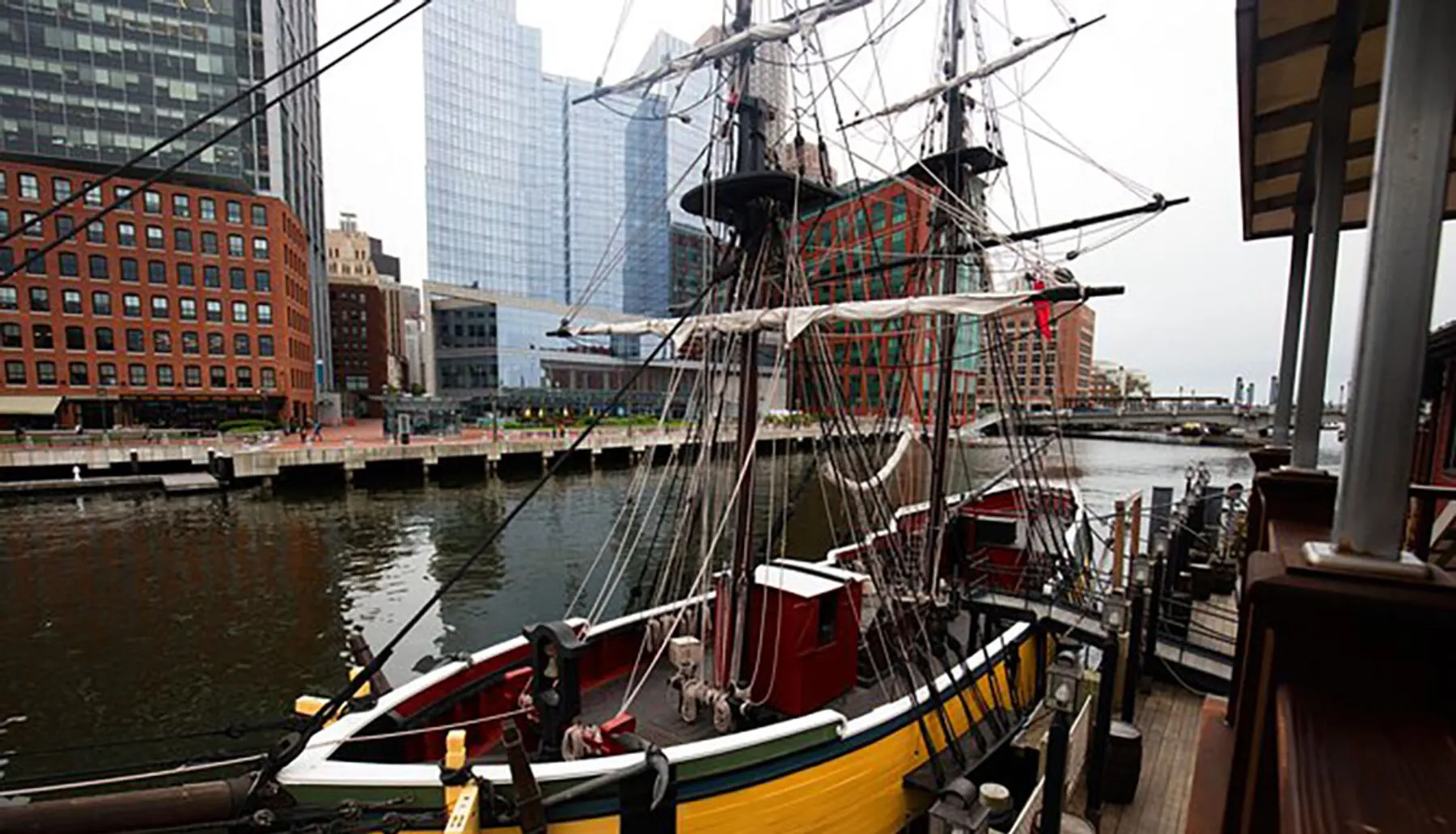 A historical tall ship is docked in a modern urban waterfront setting, blending maritime history with contemporary city architecture.