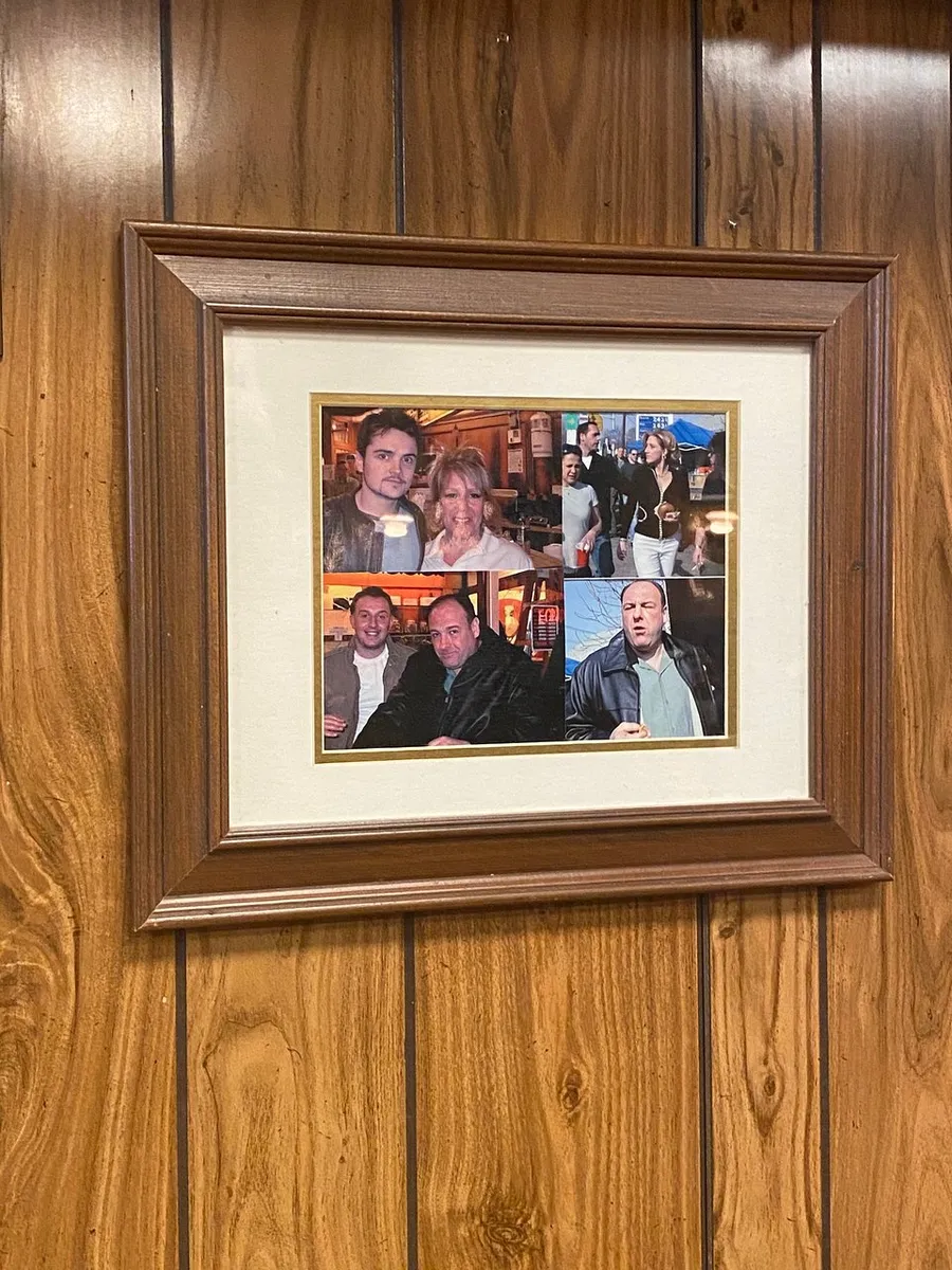 The image shows a wooden-framed collage featuring several smaller photographs of people, hung on a wood-paneled wall.