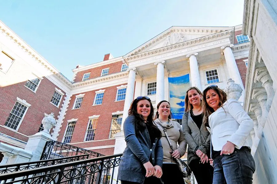 Four smiling individuals pose in front of a building with classical architecture featuring a pillared entrance and a blue banner.