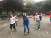 A diverse group of people appears to be joyfully participating in an outdoor dance class or activity in an urban park setting.