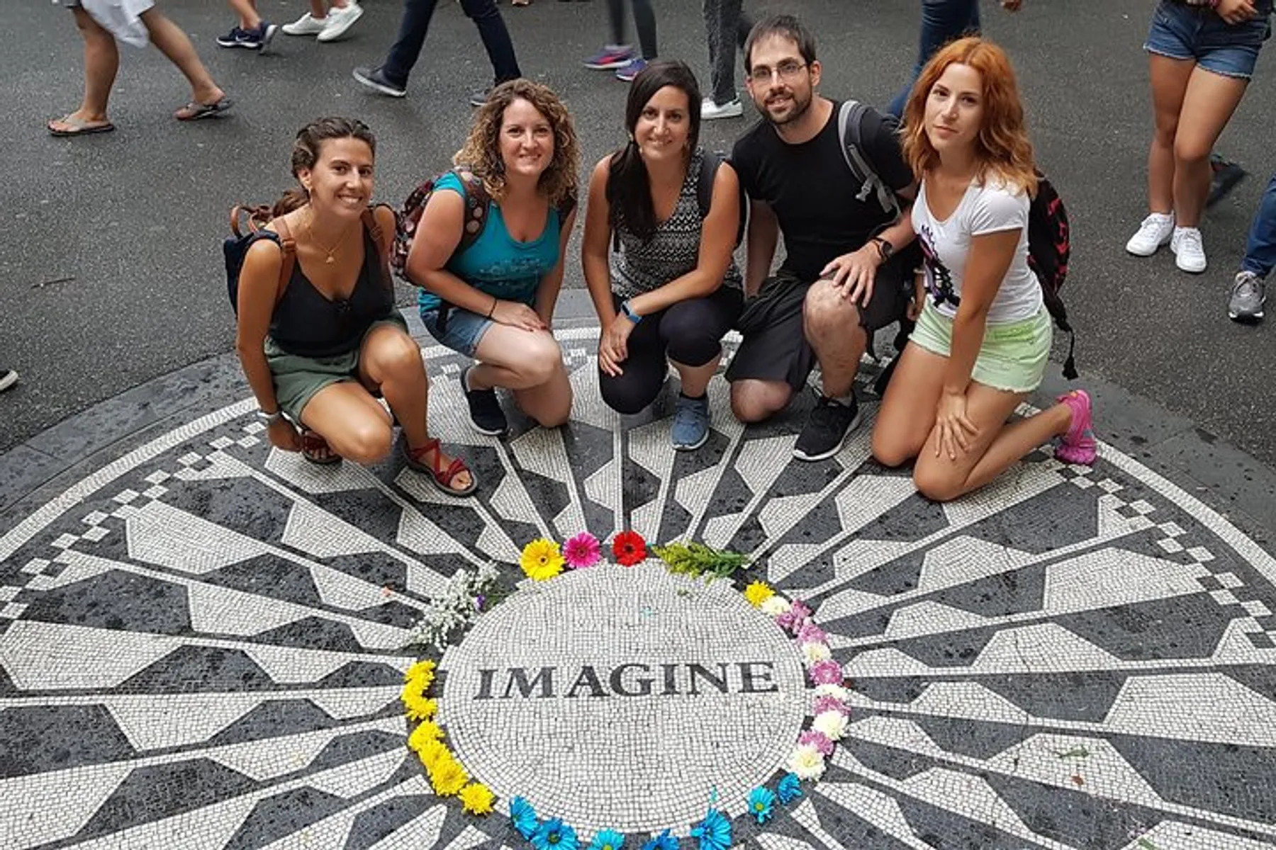Five individuals are posing for a photo around the iconic Imagine mosaic memorial in Central Park, New York City.