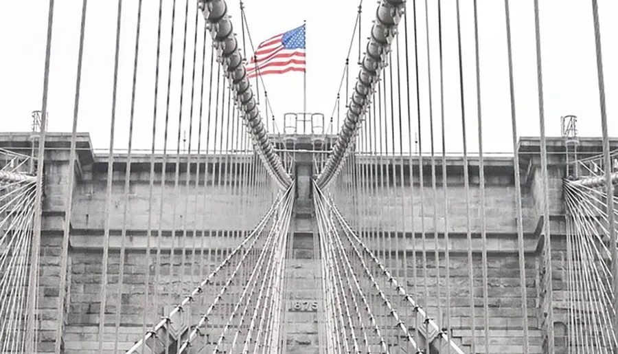 The image shows a symmetrical view of the Brooklyn Bridge's cable pattern with an American flag atop the central tower.