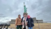 Three people are posing for a photo in front of the Statue of Liberty on an overcast day.