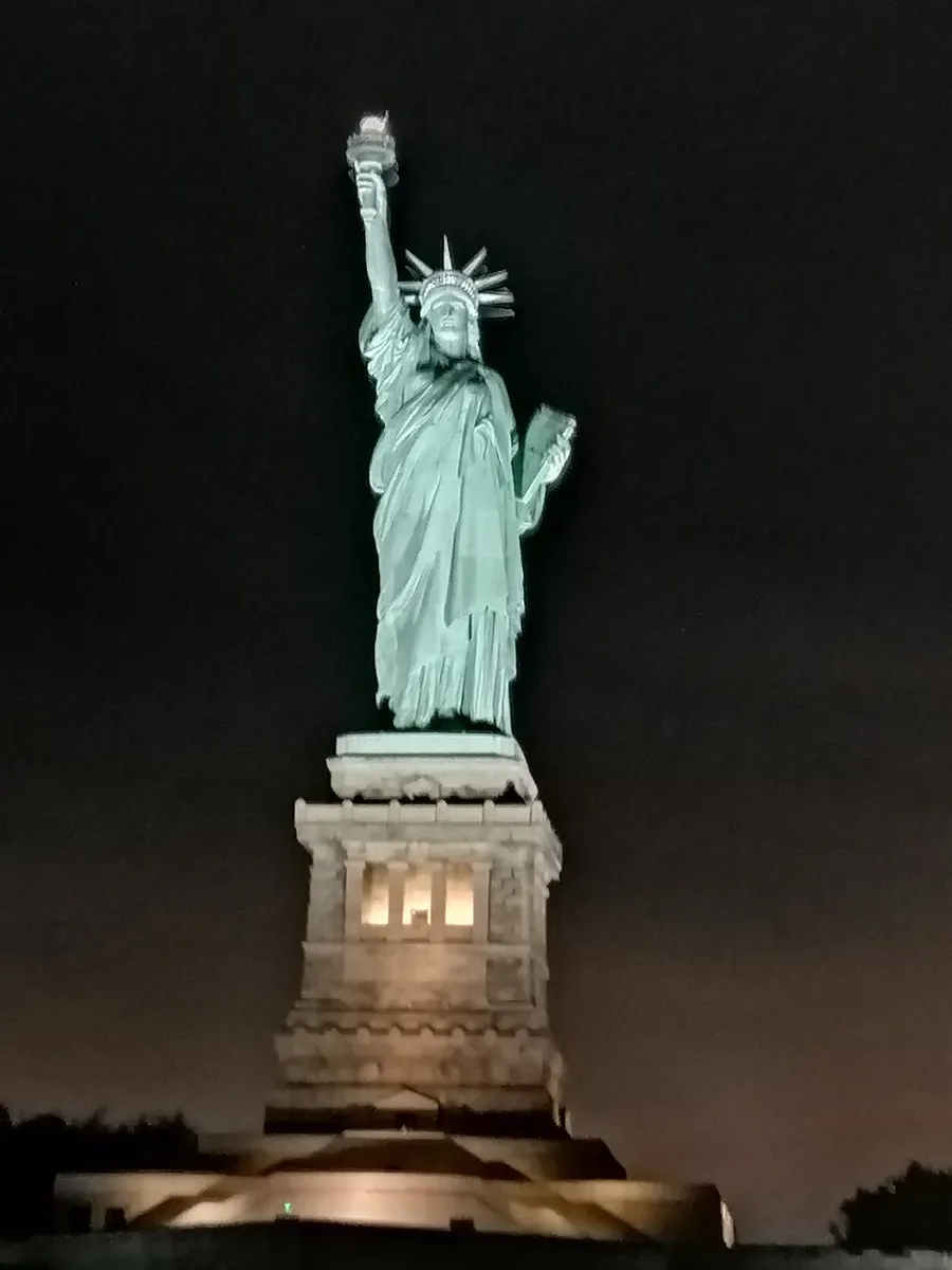 The image is a nighttime photo of the Statue of Liberty, illuminated against a dark sky.