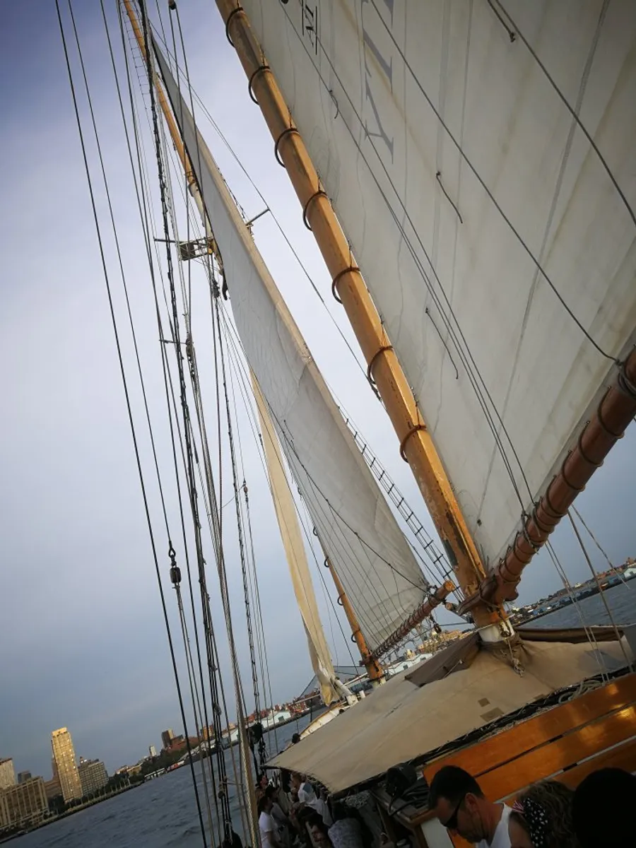 The image shows a group of people on a sailing ship with its billowing sails hoisted up the masts.