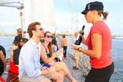 A staff member is presenting a bottle of wine to guests aboard a sailboat, indicating a leisurely and social atmosphere.