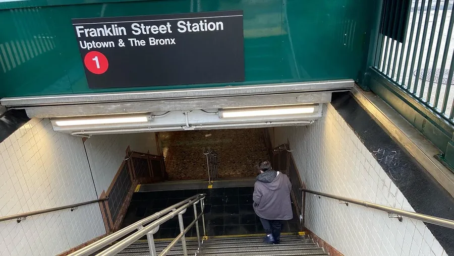 A person is descending the stairs into the Franklin Street Station entrance for uptown and the Bronx trains in the New York City subway system.