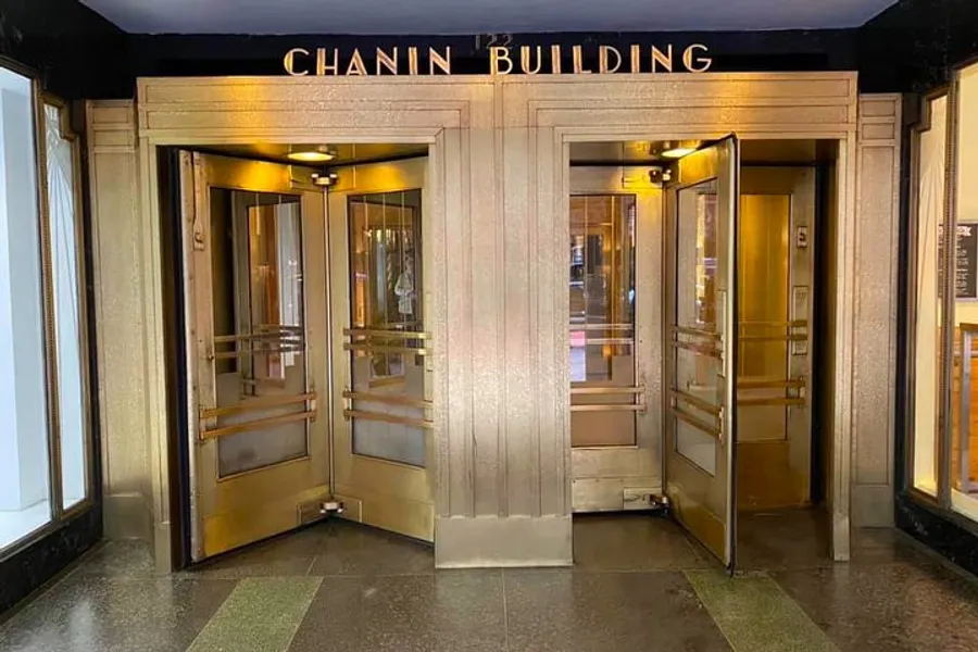 The image shows the ornate gold and brass entrance doors of the Chanin Building, featuring Art Deco style architecture.