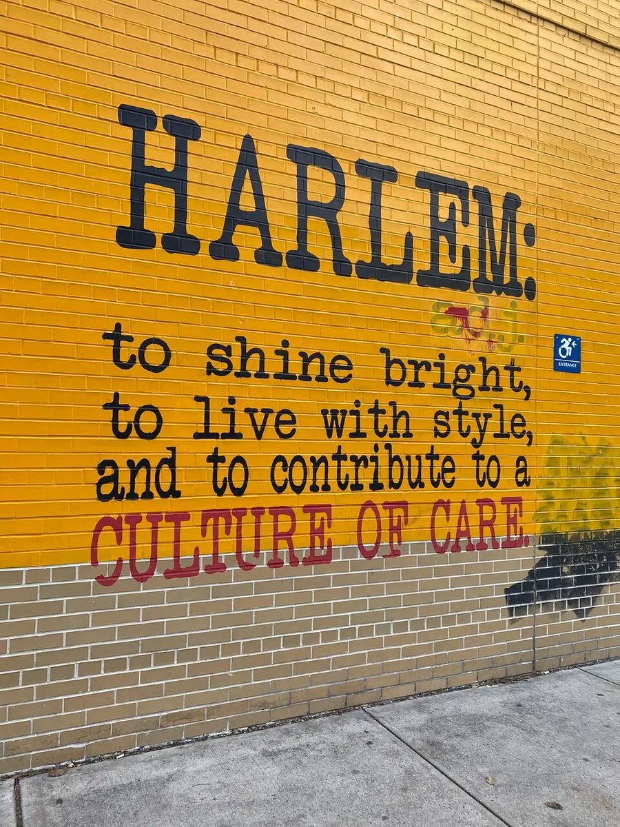 The image shows a yellow brick wall with large black letters spelling HARLEM. along with a motivational message in smaller black and red letters below, endorsing a culture of care.