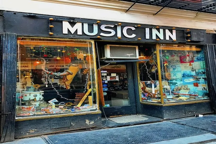 The image shows the exterior of a music store named MUSIC INN, featuring a window display filled with various musical instruments and equipment.