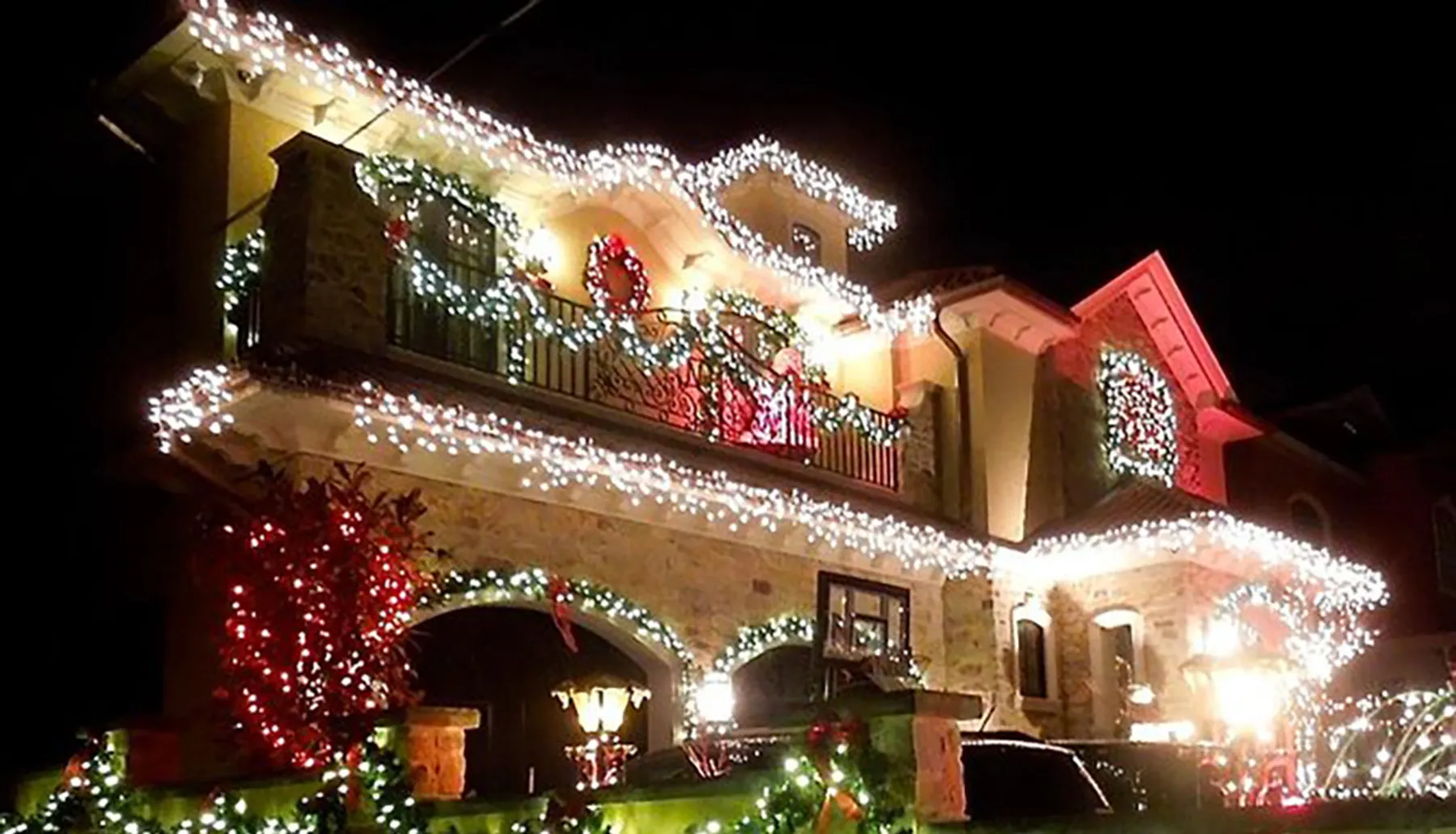 A house is festively adorned with numerous Christmas lights and decorations, creating a warm holiday atmosphere at night.