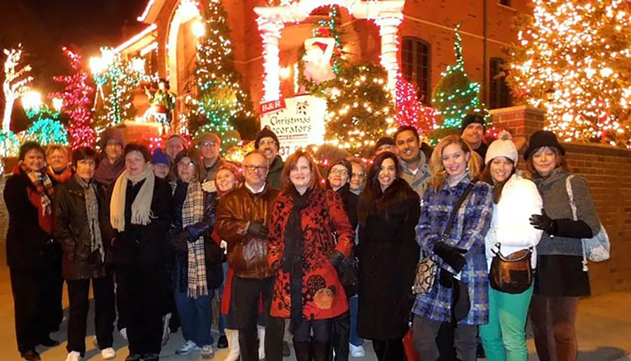A group of people are posing for a photo in front of a brightly decorated building with Christmas lights at night.