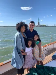 A happy family is posing for a photo on a boat with the Statue of Liberty in the background on a sunny day.