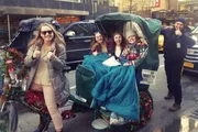 A group of cheerful people is enjoying a festive, decorated pedicab ride on a city street.