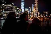 Three silhouetted individuals are gazing at a brightly lit city skyline at night across a body of water.