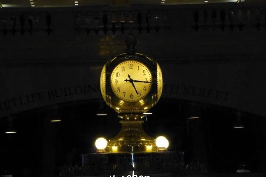 The image shows an iconic golden clock, illuminated and prominently displayed indoors, with the inscription Information visible below it.