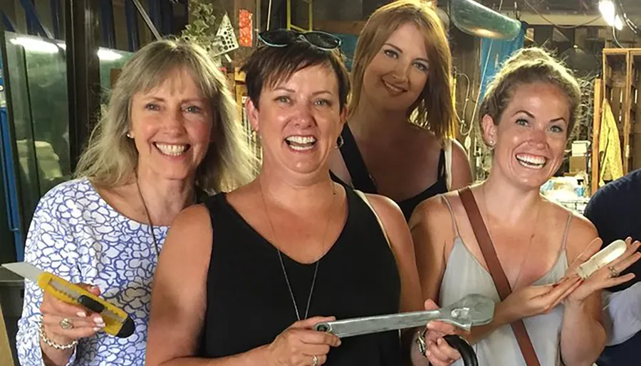 Four women are smiling for the camera while holding large sculpting chisels in a workshop setting.