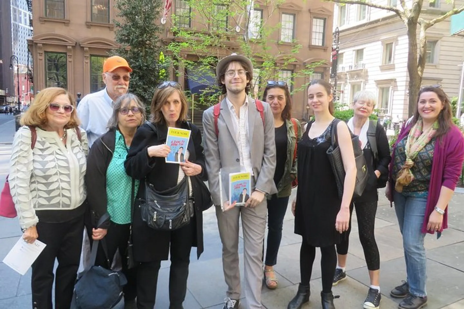 A group of people pose for a photo on a city street, two of whom are holding books with visible covers.