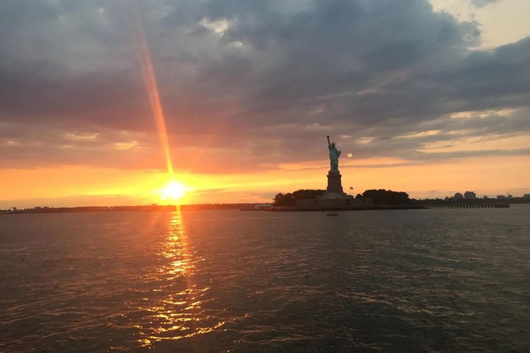 The sun sets beautifully behind the Statue of Liberty, casting a warm glow over the water.