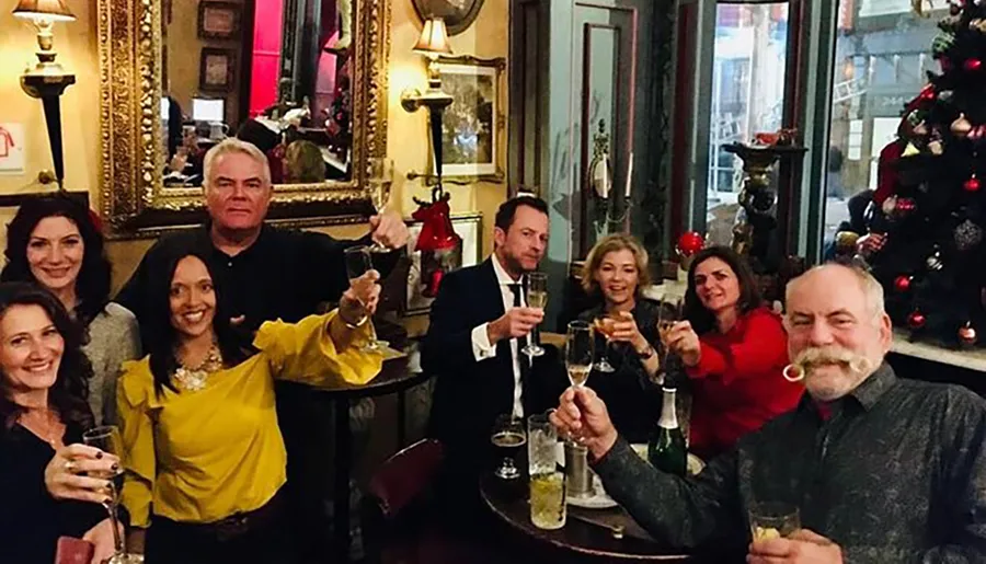 A group of people is cheerfully toasting with champagne in a decorated room with a Christmas tree in the background.