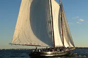 A group of people are enjoying a sail on a large, traditional sailing yacht with its sails fully billowed in the late afternoon sun.