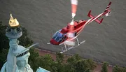 A red helicopter is flying near the Statue of Liberty.