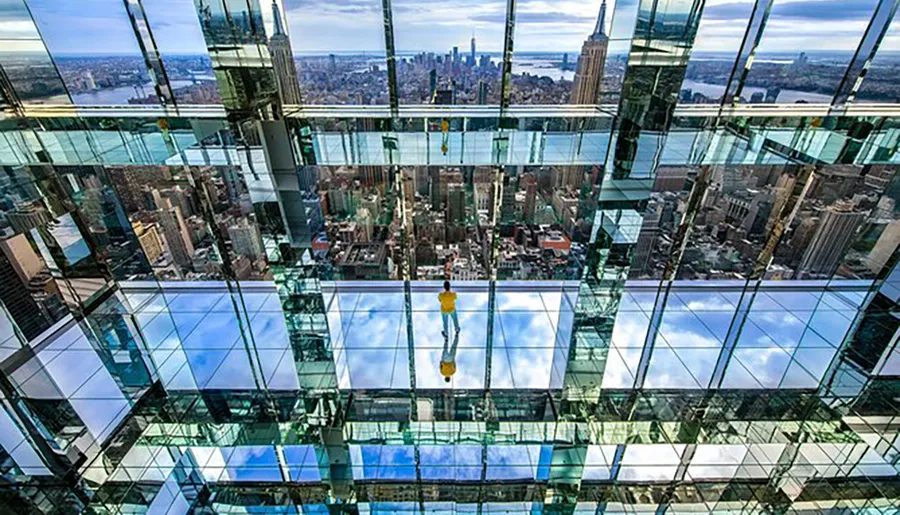 A person stands on a glass floor high above a cityscape, offering a dizzying perspective of the urban environment below.