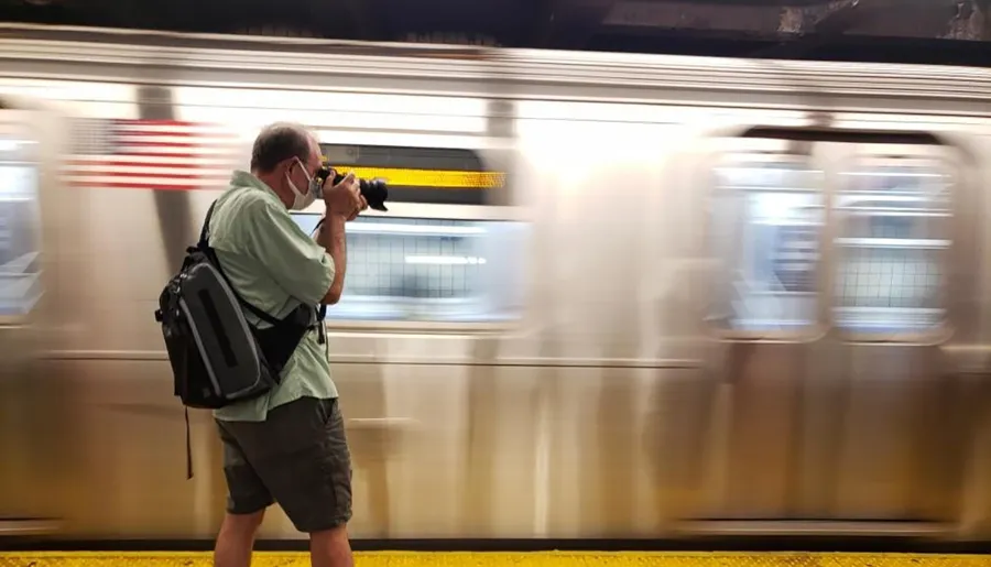 A person is taking a photograph with a DSLR camera while standing at a subway platform as a train blurs past.