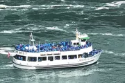 A crowded tour boat filled with passengers wearing blue ponchos is navigating a rippled body of water.