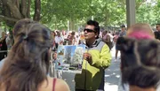 A person is holding up a poster with images of trees and text while standing outdoors in a crowd.