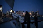 A person is gazing at the city skyline at dusk from the deck of a sailing boat.